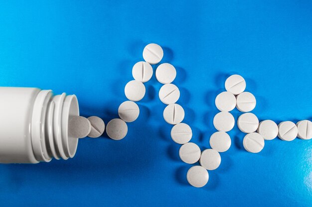 Witte medische pillen en tabletten met fles op blauwe achtergrond Close-up foto van medische preparaten met kopieerruimte