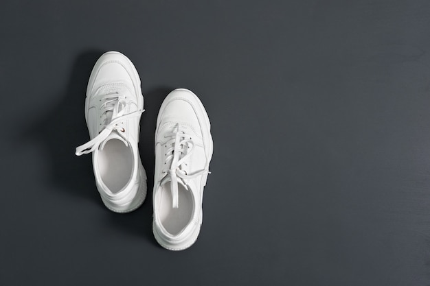 Witte moderne lederen sneakers voor dames op grijze muur achtergrond. Kopieer ruimte.