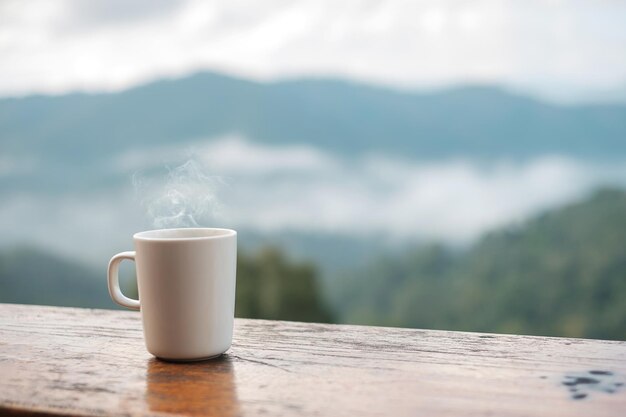 Witte mok warme koffie of thee op houten tafel in de ochtend met berg- en natuurachtergrond