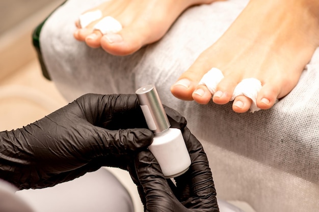 Witte nagellak in de handen van een manicure tijdens het schilderen van nagels op een vrouwelijke voeten close-up