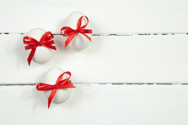 Witte paaseieren met rode linten en strikken op witte houten tafel