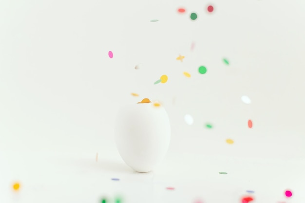 Witte paaseierschaal op lichte achtergrond met uitvliegende kleurrijke confetti Ei is een symbool van de viering van een religieuze feestdag onder katholieken, christenen en protestanten