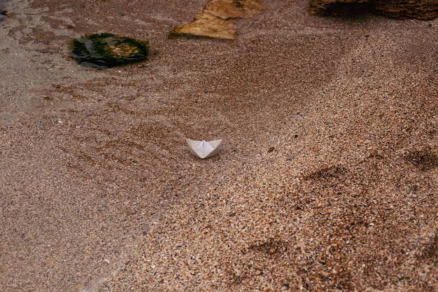 Witte papieren boot op zand in de buurt van zee op herfst of zonnige dag Kleine boot van papier op zand in de buurt van zeegolven Concept reizen toerisme vakantie rust vakantie