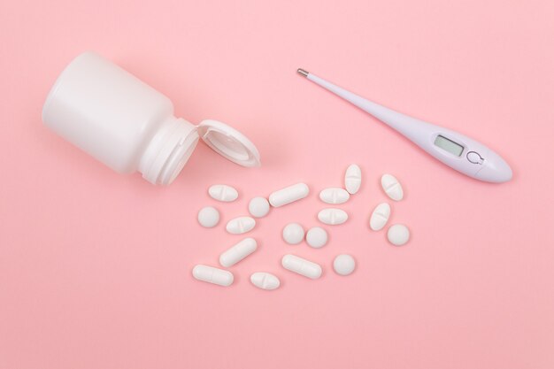 Witte pillen of tabletten met elektronische thermometer op roze achtergrond