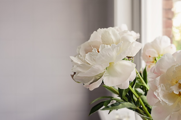 Witte pioen bloemen boeket met groene stengels en bladeren op een wazige tegel muur achtergrond