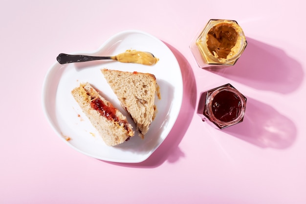 Witte plaat in de vorm van een hart met sandwiches met pindakaas en aardbeiengelei op roze achtergrond. Bovenaanzicht