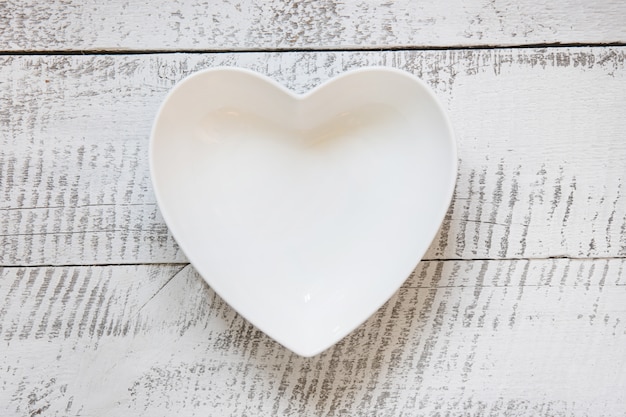 Witte plaat in vorm van hart op houten vintage tafel. bovenaanzicht.