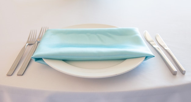 Witte plaat met een turquoise servet, metalen vork en mes, tafel instelling bruiloft