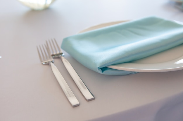 Witte plaat met een turquoise servet, metalen vork en mes, tafel instelling bruiloft