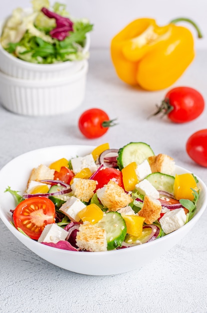 Witte plaat met mix groentesalade, groenten, crackers en sesamzaadjes op een lichte ondergrond