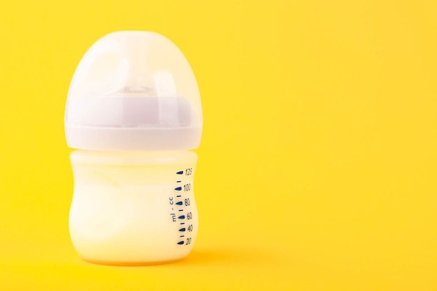 Witte plastic babyfles met fopspeen, rijk aan babyvoeding, op geel