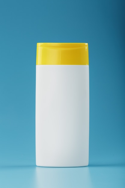 Witte plastic fles met gele dop met shampoo-gel op blauw oppervlak.