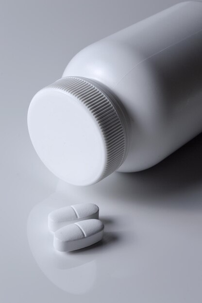 Witte plastic medicijnpot en twee witte pillen lichte achtergrond