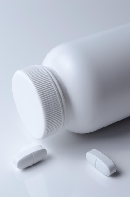 Witte plastic medicijnpot en twee witte pillen lichte achtergrond