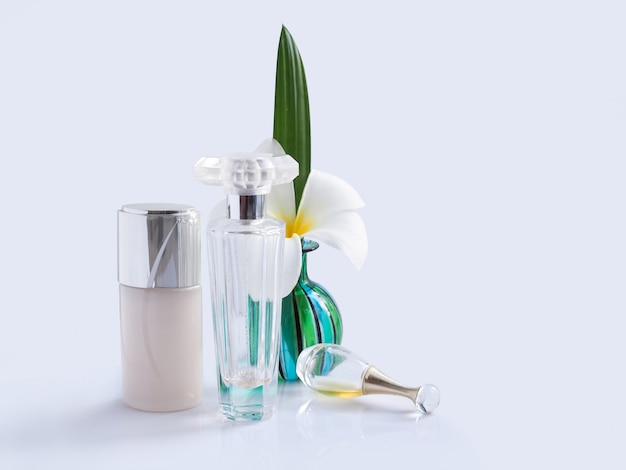 Witte plumeria spa-bloem in groene glazen vaas met transparante parfumflesjes en lotionfles.