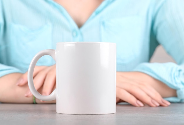 Witte porseleinen koffiemok mockup op de grijze stenen tafel met meisje in blauw shirt achter