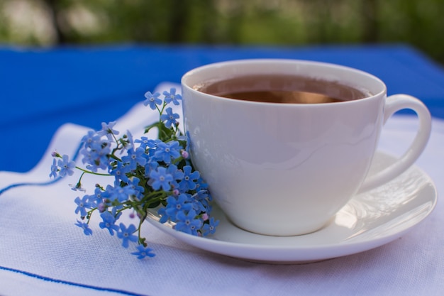 Witte porseleinen kop met thee op tafel met blauw tafelkleed en wit servet