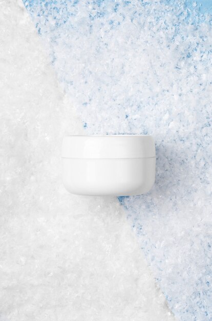 Witte pot met gezichtscrème op een witte en blauwe achtergrond met kunstmatige sneeuw