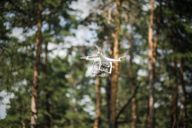 Witte quadrocopter vliegt tegen de achtergrond van een groen bos