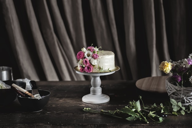 Witte romige cake versierd met rozen in donker interieur