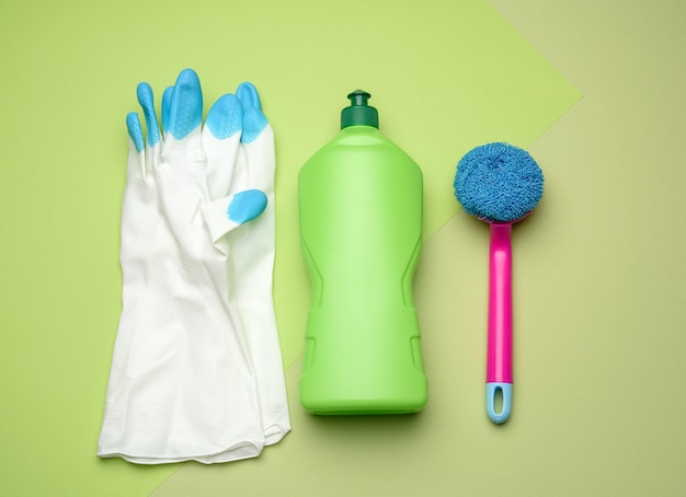 Witte rubberen handschoenen voor het reinigen, roze borstels en reinigingsvloeistof in een plastic fles op groen, bovenaanzicht