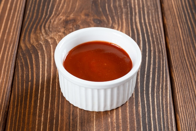 Foto witte sauskom van pikante tomatensaus op houten tafel