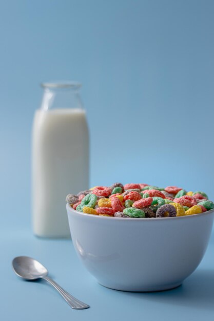 Foto witte schaal met kleurrijke ringvormige granen en melk op een blauwe achtergrond
