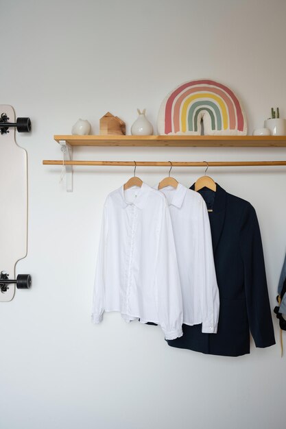 Witte shirts en een blauwe jas hangen op een houten plank in de tienerkamer.
