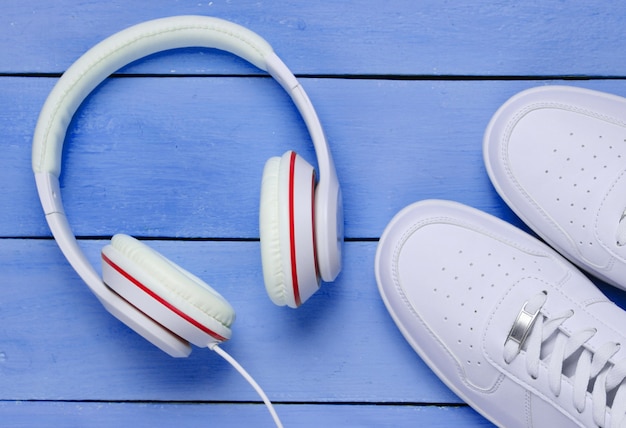 Witte Sneakers met koptelefoon op blauwe houten achtergrond. Muziekconcept. Platliggend, minimaal.