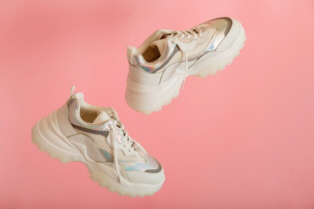 Witte sneakers vliegen. Vrouwelijke witte lederen schoenen op roze achtergrond. Paar stijlvolle urban sneakers