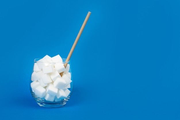 Witte suikerklontjes in een glas met een rietje en op een blauwe achtergrond