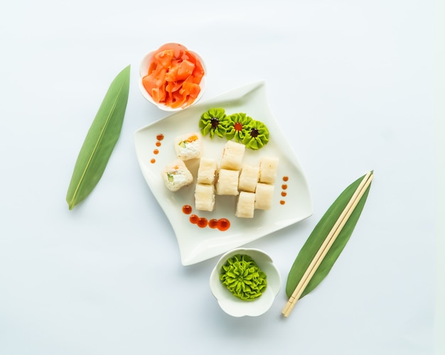 Witte sushi op een witte plaat en wit oppervlak met wasabi, gember en chopstocks