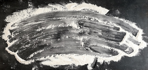 Witte tarwemeel verspreid over een zwarte tafel