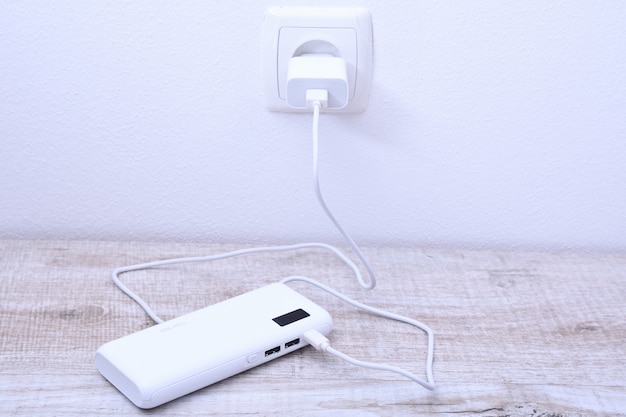 Witte telefoon power bank aangesloten op de aansluiting op de muur voor het opladen op houten tafel