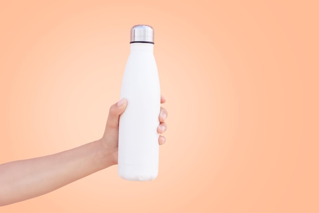 Witte thermo-fles in de hand op de achtergrond van de kleur van het jaar perzik fuzz