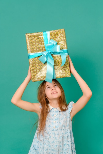 Witte tiener met een blauwe jurk houdt een geschenkdoos boven haar hoofd op een groen oppervlak