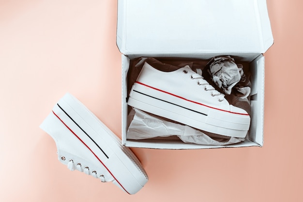 Witte trendy witte sneakers in kartonnen doos op romige perzik achtergrond