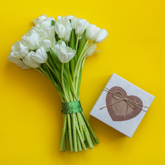 Witte tulpen en geschenkdoos op heldere gele achtergrond. Lente concept.