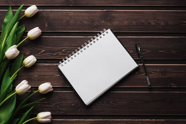 Witte tulpen op een houten tafel met een lege laptop. Plat lag, bovenaanzicht samenstelling