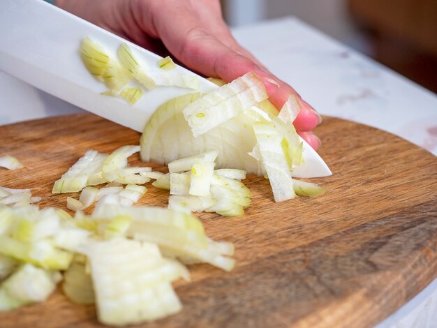 Witte uien worden gesneden met een mes op een houten bord. Het concept van koken.