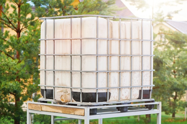 Witte vierkante watertank op metalen frame geïnstalleerd op de achtertuin voor het besproeien van de tuin Witte enorme container voor vloeistof met metalen rooster Indastrial vloeistofreservoir versterkt een metalen rooster