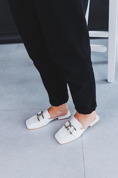 Witte vrouwelijke leren pantoffels close-up op vrouwelijke benen Nieuwe collectie leren zomerschoenen voor dames