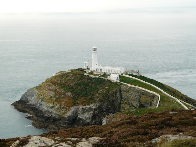 Witte vuurtoren aan de rand van een land en kalme zee op de achtergrond in Wales