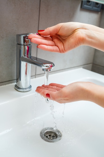 Witte wastafel met een zilveren kraan in de badkamer. Grijs blikje met vloeibare zeep voor de handen. Kraanwater opendraaien, persoonlijke handhygiëne. Handen wassen onder stromend water