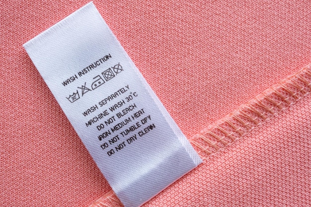 Witte wasverzorging wasinstructies kledinglabel op roze katoenen shirt