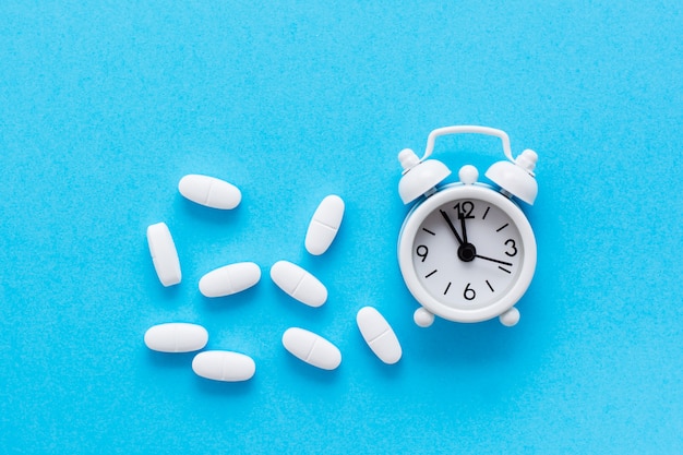 Witte wekker en witte ovale pillen ernaast op een blauwe achtergrond