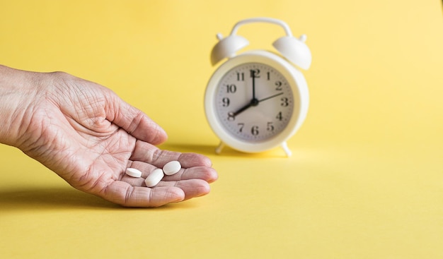 Witte wekkertabletten op een gele achtergrond Hand van een vrouw die pillen neemt Concept van gezondheidszorg en medicijnen