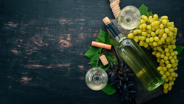 Witte wijn in een fles met een glas en druiven Op een zwarte houten achtergrond Vrije ruimte voor tekst Bovenaanzicht