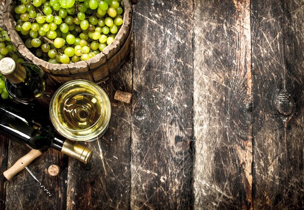 Foto witte wijn met een emmer groene druiven. op een houten tafel.