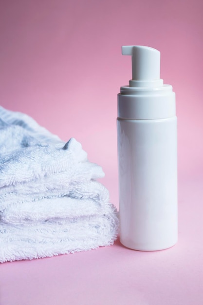 Witte zeepfles met pompmodel met handdoek op roze achtergrond. Dispenser voor cosmetische plastic flessen